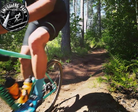 Rider on a green gravel bike takes a sandy forest trail at Smugglers Path, the Belgian gravel event.