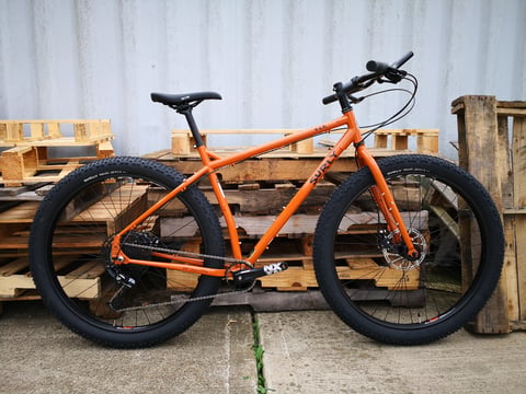 Orange 2019 Surly ECR in profile with Knard 29 x 3.0 tyres, parked against pallets and a corrugated wall.