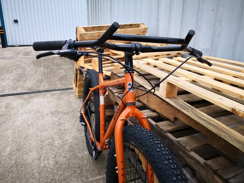 Front view of the Surly ECR's wide black handlebar, brake levers and orange fork beside stacked pallets.