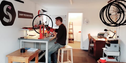 Ben Sharp trues a wheel on a red stand in his Sharp Precision Wheels workshop.