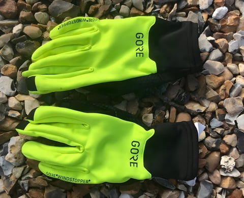 Pair of neon yellow Gore Wear Gore-Tex Infinium gloves with black cuffs lying on shingle.