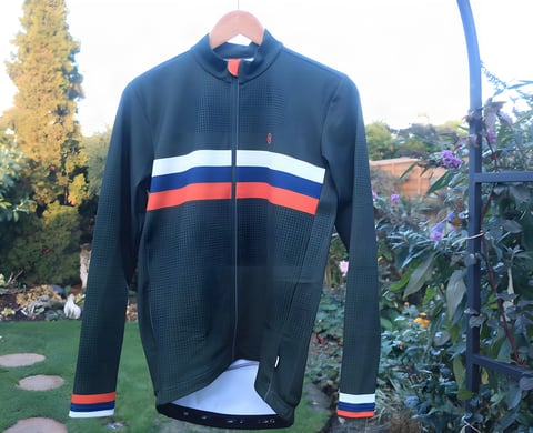 Chapeau Club Thermal Jersey in green with white, blue and orange chest stripes, hanging in a garden.