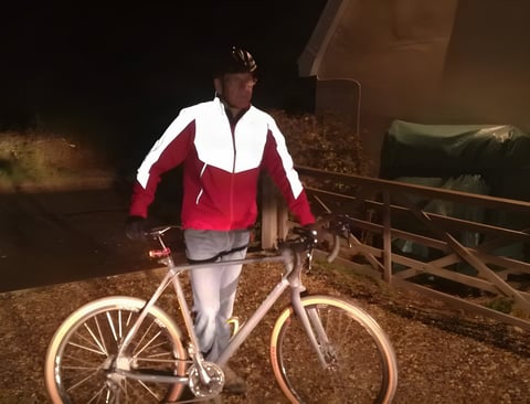 A cyclist in the red Altura Nightvision Thunderstorm Jacket stands with a bike at night, reflective panels lit white.