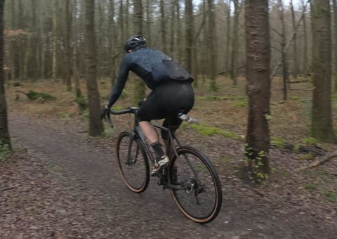 Rider in Alpkit Rhythm 3/4 Bibtights on a gravel bike along a leafy forest track in winter.