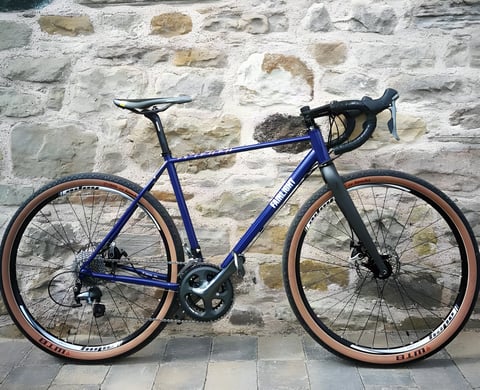 Mark Downie's blue Fairlight Secan gravel bike with tan-wall WTB tyres against a stone wall.