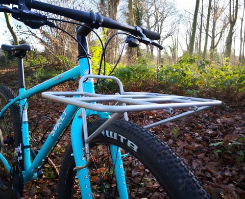 Surly 24-Pack Rack in silver fitted to the fork of a turquoise Bridge Club among autumn leaves.