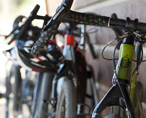 Green Salsa gravel bike with SRAM drop bars and patterned bar tape, other bikes blurred behind it.