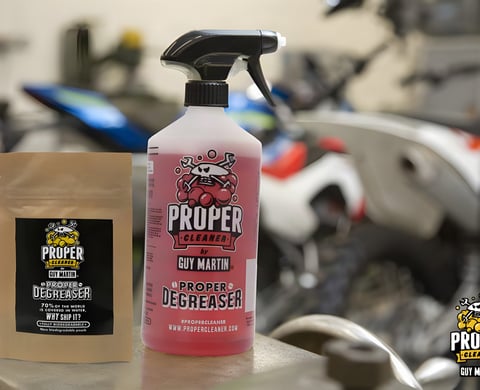 Guy Martin Proper Degreaser trigger bottle of pink liquid beside the brown refill pouch, with a workshop behind.