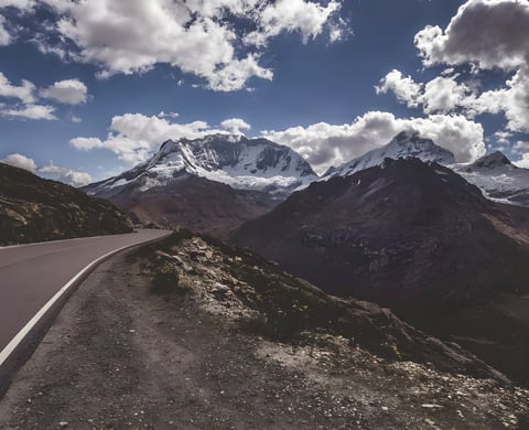 Empty paved road curves below snow-capped Andean peaks on the BikingMan Peru route.