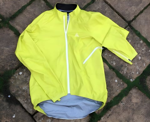 Rider in a neon yellow 7Mesh Rebellion waterproof jacket and white helmet, standing in front of a gravel bike.