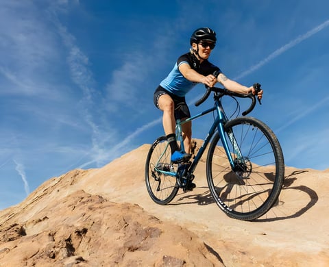 Rider on the 2019 All-City Cosmic Stallion in teal paint pauses on a sandstone outcrop under a blue sky.