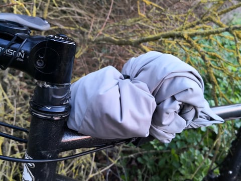 Rolled grey windproof jacket stowed on the top tube with the Super 8 strap, next to the stem.