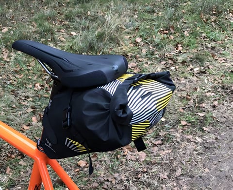 Apidura Racing Saddle Pack, 5L, mounted on an orange bike in leaf-strewn grass.