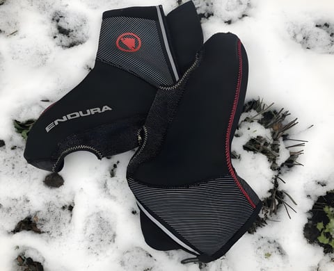 Pair of black Endura Freezing Point overshoes with red logo and reflective trim lying on snow.
