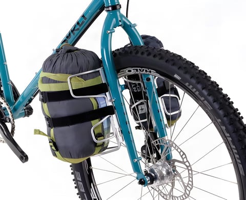 Pair of silver Passport Cycles Lug-Kages on a teal Surly fork, each holding a stuff sack, on a white background.