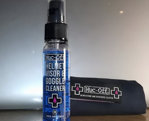 Muc-Off Helmet, Visor and Goggle Cleaner spray bottle beside its ultra fine microfibre cloth.