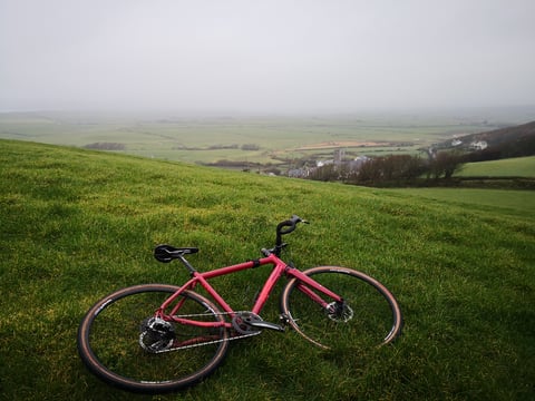 Sonder Camino AL lying on a grassy hillside above a misty valley with a church and farmland.