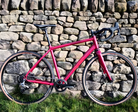 Red Sonder Camino AL gravel bike with SRAM Rival 1 and tan-wall tyres, leaning against a dry-stone wall.