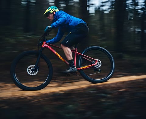 Rider in a blue jacket speeds a red Sonder Transmitter plus-tyred hardtail along a forest trail.
