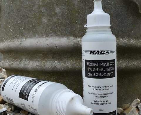 Two 250ml bottles of Halo Fibre-Tech Tubeless Sealant, one upright and one lying on stones.