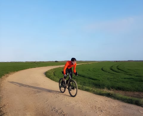 Josh Ibbett rides his Mason ISO along a curving gravel track through green fields under a clear blue sky.
