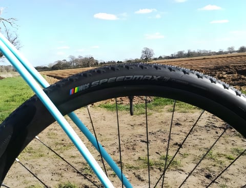 Ritchey WCS Speedmax tubeless-ready tyre on a wheel with a teal frame tube, in front of a ploughed field.