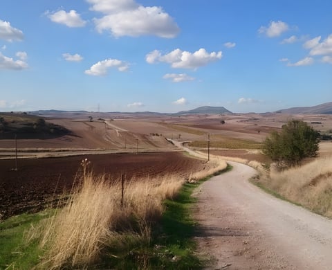 Empty gravel road winding through ploughed fields towards distant hills, the kind of route HUNT Beyond covers.
