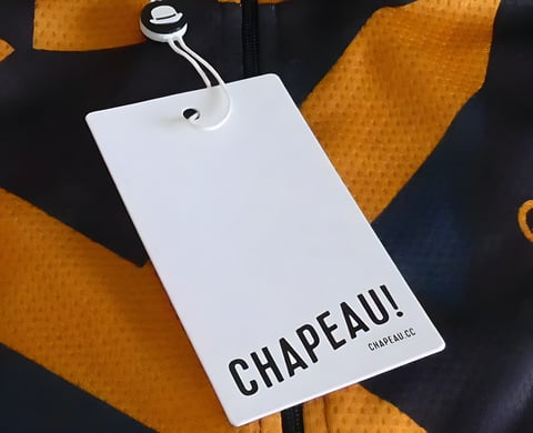 A Chapeau branded swing tag attached to an orange and navy patterned jersey.