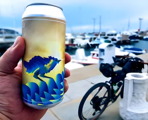 Hand holding a can of craft beer by a harbour, loaded bike behind, on a beerpacking trip through Slovenia and Croatia.