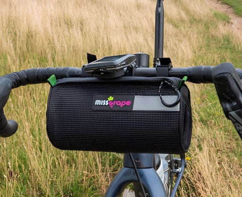 Miss Grape Moon handlebar bag strapped to the drop bars of a gravel bike, with a GPS computer mounted above it.