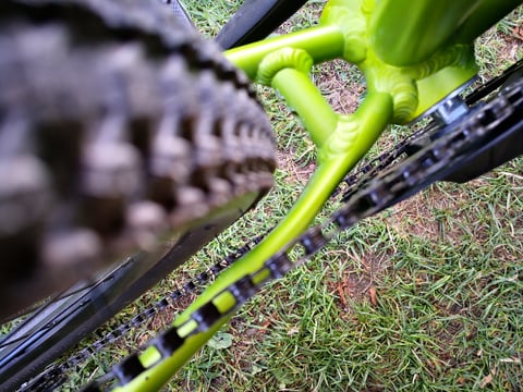 Looking along the green chainstays of the Bombtrack Beyond Junior towards the chain and blurred rear tyre.