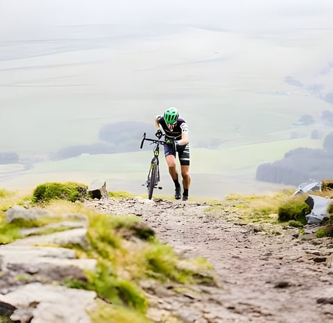 Rider pushes a cyclocross bike up a rocky fellside path above a misty valley at the 3 Peaks Cyclocross in the Dales.