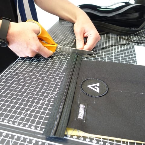 Scissors trim a zip on a black Cordura panel with a round patch and Straight Cut label on a cutting mat.