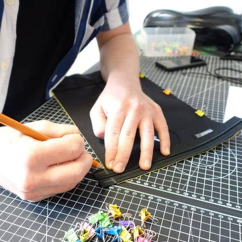 Pencil marking a zip line on black fabric on a cutting mat, with colourful clips nearby, at Straight Cut.