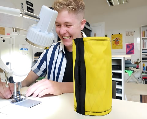 Straight Cut founder Ross O'Reilly laughs at his sewing machine beside a finished yellow bikepacking bag.