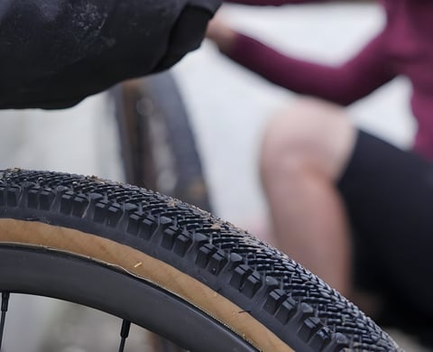 Close-up of a WTB Venture 40 gravel tyre with tanwall sidewall on a wheel, a rider blurred behind.