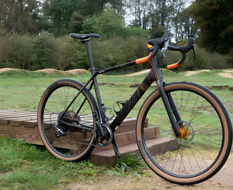 Salsa Warroad Carbon Force 1 650b in black with orange details, parked beside dirt mounds in a bike park.