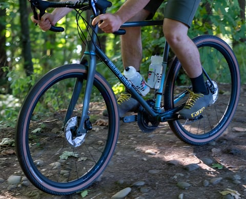 Rider on a Breadwinner gravel bike with Roval Terra carbon wheels and tan-wall tyres on a rocky wooded trail.