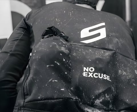 Mud-spattered rider's back with a Scope logo and "No Excuse" slogan at the Backyard Breakaway gravel ride.