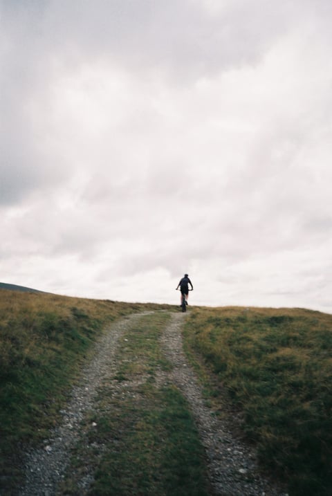 Lone rider crests a hill on a stony double-track under a heavy grey sky in the Lake District.