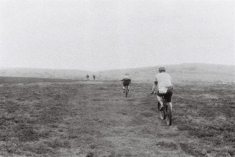 Four riders head away across open misty moorland on the Low Key Lakes Weekender, in black and white.