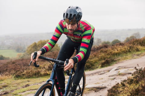CX Syndicate rider in long-sleeve team kit and a POC helmet climbs a rocky moorland track.