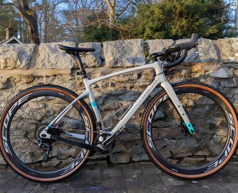 Scope R4A wheels on a grey and teal Chapter2 gravel bike leaning against a stone wall.