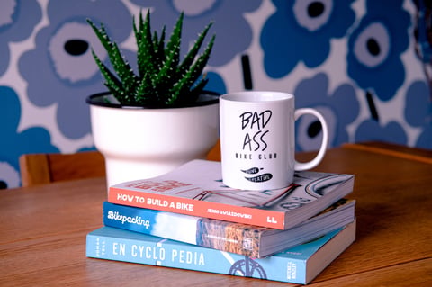 Rune Creative Bad Ass Bike Club mug on a stack of cycling books including Bikepacking and En Cyclo Pedia.