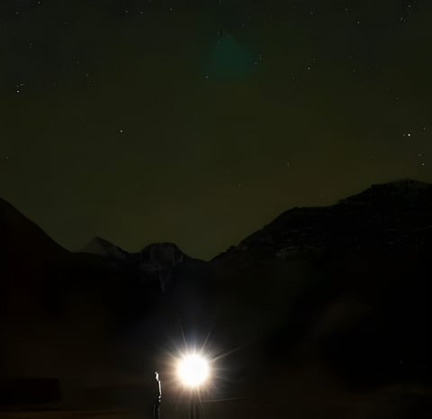 A figure stands in torchlight beneath a starry night sky and dark mountains in the Pamirs, Tajikistan.