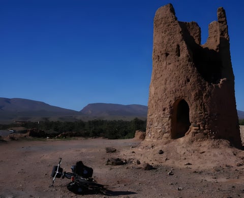 A loaded bikepacking bike lies beside a ruined mud-brick kasbah tower in Morocco, where the Atlas Mountain Race is run.