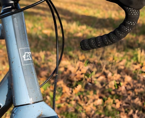 Kinesis G2 head tube in slate blue with the K logo, reflective-dot bar tape and autumn leaves behind.