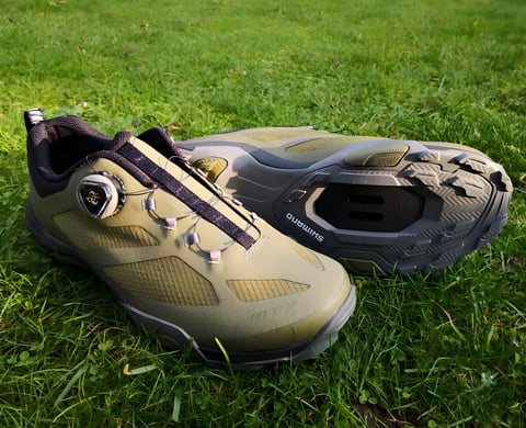 Shimano MT-7 SPD shoes in olive green with a BOA dial, one shown upright and one on its side to show the sole.