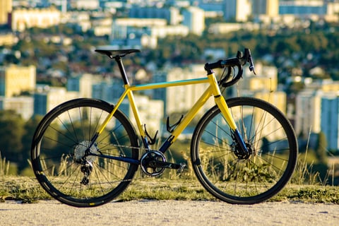 Yellow and navy Wish One SUB steel gravel bike in side view, with a city skyline behind.