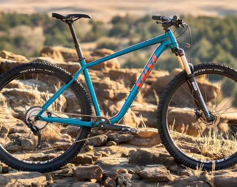 A teal Salsa Rangefinder hardtail with WTB Trail Boss tyres stands on rocky ground.